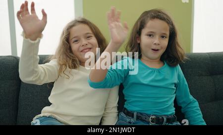 Two kids sitting on sofa speaking and saying hello with hand at home Stock Photo
