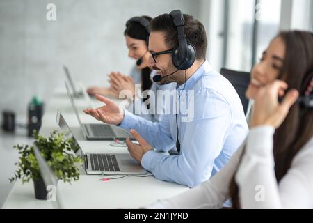 Side view portrait of handsome male IT support executive agent talking to customer while working in call center. Stock Photo