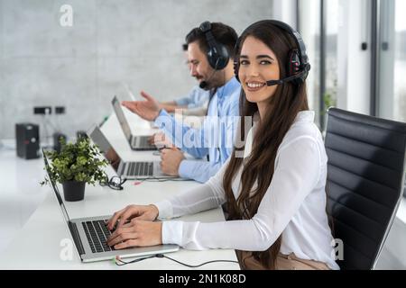Portrait of smiling young female call center operator wearing headphones working in customer support service. Stock Photo
