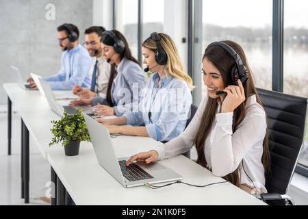 Group of friendly professional customer support operators interacting with clients while having online chats at call center office. Stock Photo