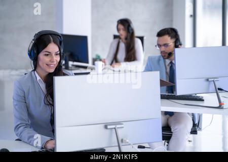 Beautiful customer support representative woman using computer in zig zag customer service office. Stock Photo