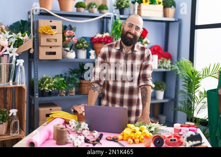 Young bald man florist smiling confident using laptop at flower shop Stock Photo