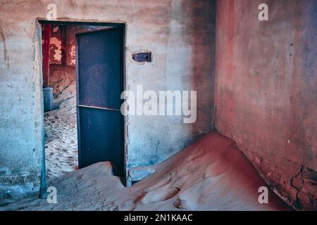 Old store-room storeroom in the bakery at Kolmanskop Ghost Town, Namibia.There's a rusted metal door and peeling wall paint. Creative, processed image. Stock Photo