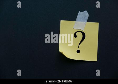 Yellow paper attached to the black wall written with question symbol. Stock Photo