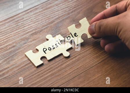 A hand holding puzzle pieces with word possible spread over two section. Concept of problem solving and overcoming challenges. Stock Photo