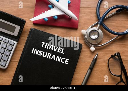 Top view of glasses, passport, stethoscope, airplane toy, calculator, pen and notebook written with Travel Insurance. Stock Photo
