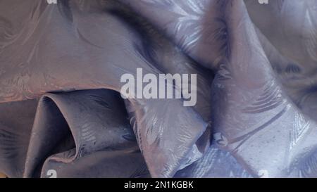 curved in smooth waves blue shiny textile material of silver-blue color with a floral pattern as an abstract discreet background Stock Photo