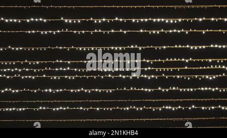 strands of street garlands with small bulbs in the dark air of the night as a magical blurred background on the theme of the celebration, party bokeh Stock Photo