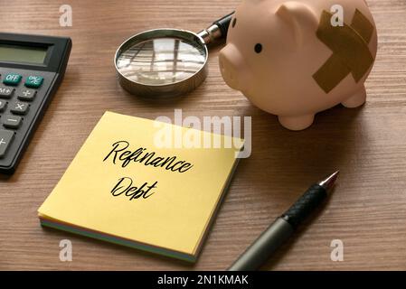 Selective focus of calculator, magnifying glass, piggy bank, pen and memo note written with Refinance Debt on wooden background. Stock Photo