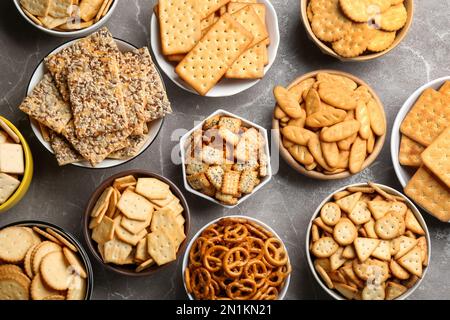 Different delicious crackers in bowls on grey table, flat lay Stock Photo