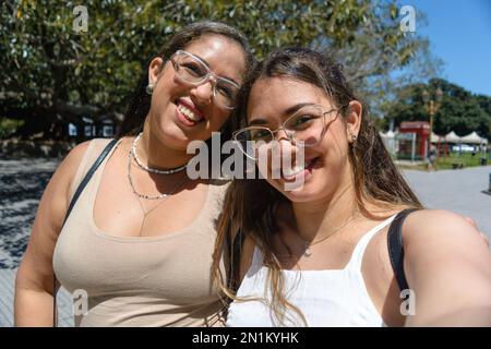selfie portrait of mother and daughter young latina tourists of venezuelan ethnicity, happy smiling looking at the camera, on the street walking throu Stock Photo