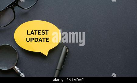 Top view of glasses, pen, magnifying glasses and yellow speech bubble written with Latest Update on black background with copy space. Stock Photo