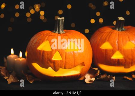 Pumpkin jack o'lanterns, candles and autumn leaves on table against blurred background. Halloween decor Stock Photo