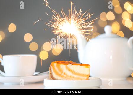 Cake with burning sparkler on table against blurred festive lights Stock Photo