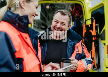 Rescuers having break in front of ambulance car, talking and drinking coffee. Stock Photo