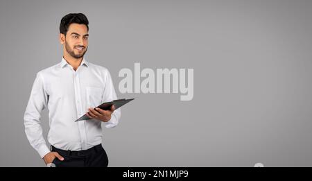 Portrait Of Handsome Young Arab Businessman With Clipboard In Hands Stock Photo