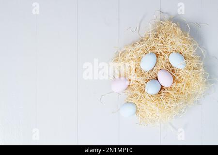 Pastel pink and blue Easter eggs in a nest on a white wooden background. Top view with copy space Stock Photo