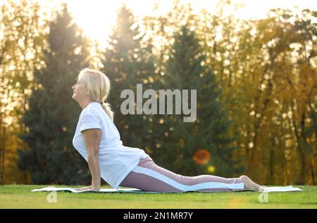 Mature woman practicing yoga on green grass in park Stock Photo