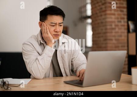Sad middle aged man employee working on laptop at home office, looking at computer screen, copy space Stock Photo