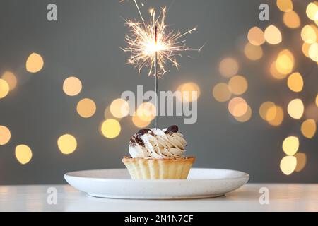 Cupcake with burning sparkler on table against blurred festive lights Stock Photo