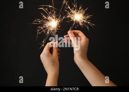 Woman holding bright burning sparklers on black background, closeup Stock Photo