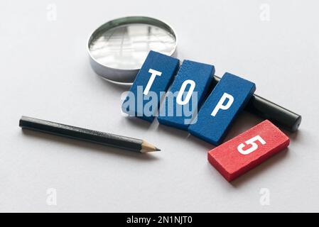 Pencil, magnifying glass and wooden block written with Top 5 on white background. Stock Photo