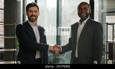 Two happy smiling diverse multiracial businessmen multiethnic partners men Caucasian and African American business people in office shaking hands Stock Photo