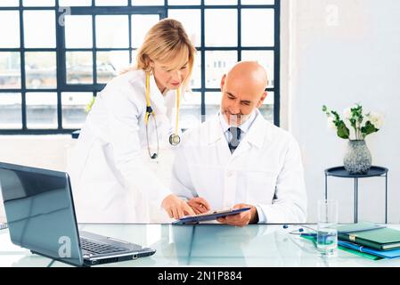 Shot of male doctor sitting at desk while female doctor standing next to him and consulting. Group of medical team working together in the doctor’s of Stock Photo