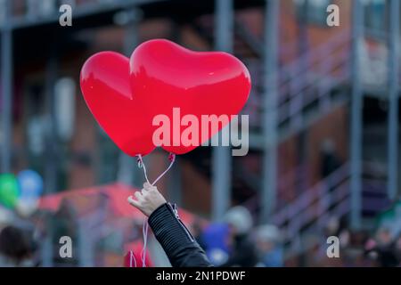 Two LED balloons in the form of scarlet burning hearts in evening in girl's hand. Romantic background, Valentine's Day Stock Photo