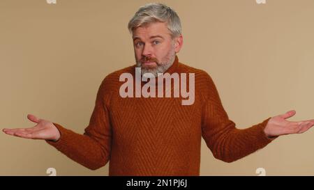 I dont know what to say. Confused middle-aged man feeling embarrassed about ambiguous question, having doubts, no idea, being clueless, uncertain. Senior guy isolated on beige studio wall background Stock Photo