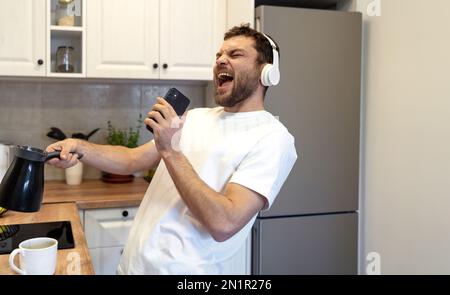 Man in headphones making coffee in morning listening music and singing alone. Stock Photo