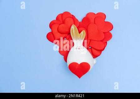 A red heart made up of small hearts and a white rabbit on a blue background. The minimum concept of a holiday. Valentine Card Stock Photo