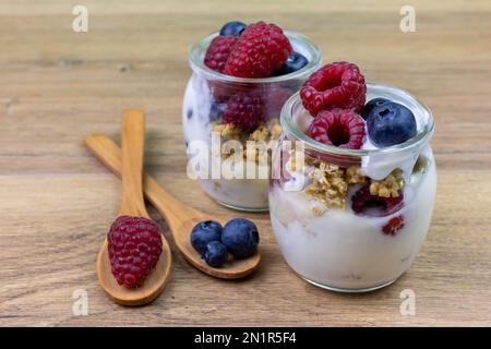 glass cups of yogurt with muesli, blueberries and raspberries on wooden table Stock Photo