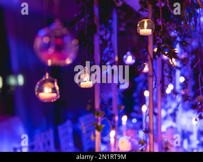 Candles in small glass circlular candle holders handled on strings. Beautiful decorations in blue electric light. Stock Photo