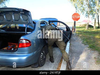 Soldier searching personal belongings of suspect in a stopped car. Checkpoint, training. Military base, Ukraine Stock Photo