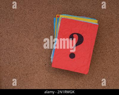 A stack of colorful paper notes with question marks on them on a cork board. Close up. Stock Photo