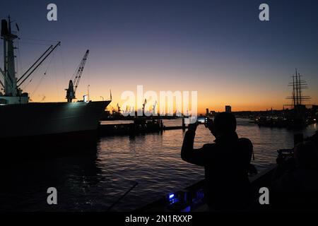 Hamburg, Germany. 06th Feb, 2023. A man photographs the evening atmosphere during sunset on the Jan Fedder promenade in the harbor. Credit: Marcus Brandt/dpa/Alamy Live News Stock Photo