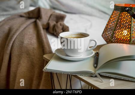 Cozy home setting with cup of coffee, notebook and table lamp. Home coffe break , modern cozy interior setting Stock Photo