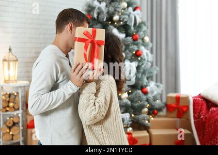 Couple kissing while hiding behind Christmas gift at home Stock Photo