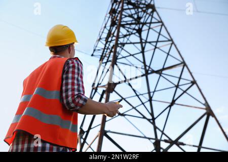 Electrical engineer with walkie talkie near high voltage tower, low angle view Stock Photo