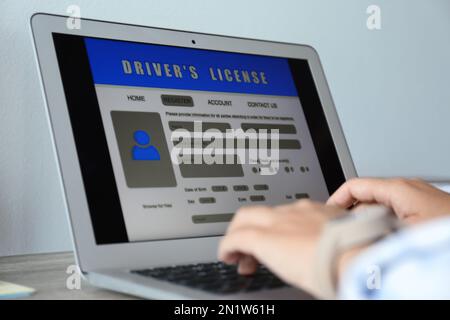 Woman using laptop to fill driver's license application form at table, closeup Stock Photo