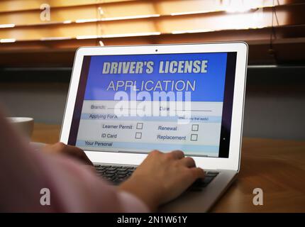 Woman using laptop to fill driver's license application form at table indoors, closeup Stock Photo