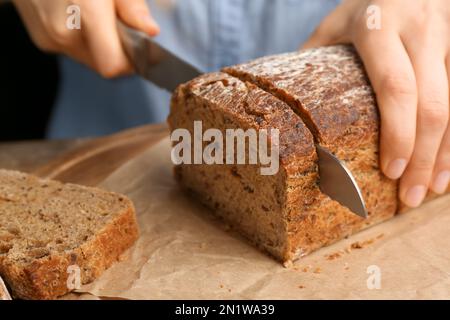 Woman cutting freshly baked bread at table, closeup Stock Photo