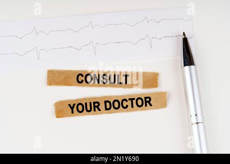 Medical concept. On the cardiogram lies a pen and torn paper with the text - Consult your doctor Stock Photo