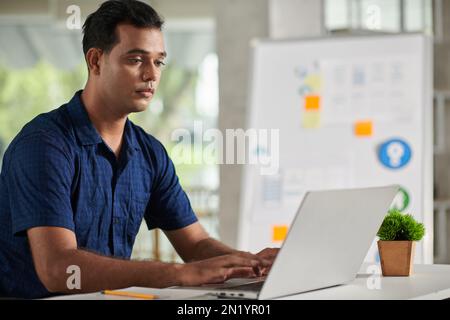 Portrait of UX designer working on laptop in modern office, creative website interface Stock Photo