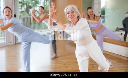 Active positive senior woman performing dance elements during lesson with female group in modern school for adults Stock Photo