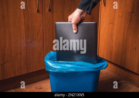 A man throws a laptop in the trash. Man's hand with a laptop and a trash can in blue.. Stock Photo