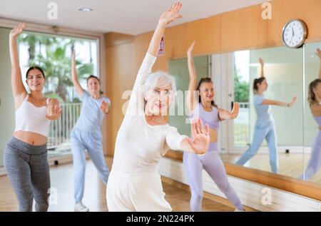 Active positive senior woman performing dance elements during lesson with female group in modern school for adults Stock Photo