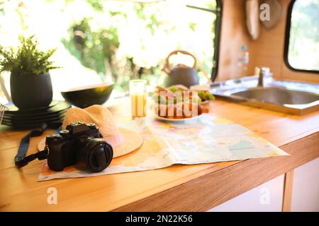 Camera, hat and world map on wooden table in modern trailer. Camping vacation Stock Photo