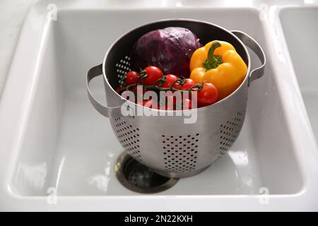 Colander pot with fresh vegetables in kitchen sink Stock Photo